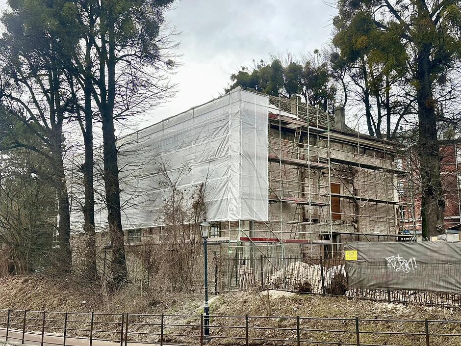 na zdjęciu stary budynek z którego skuwany jest tynk, jest częściowo osłonięty