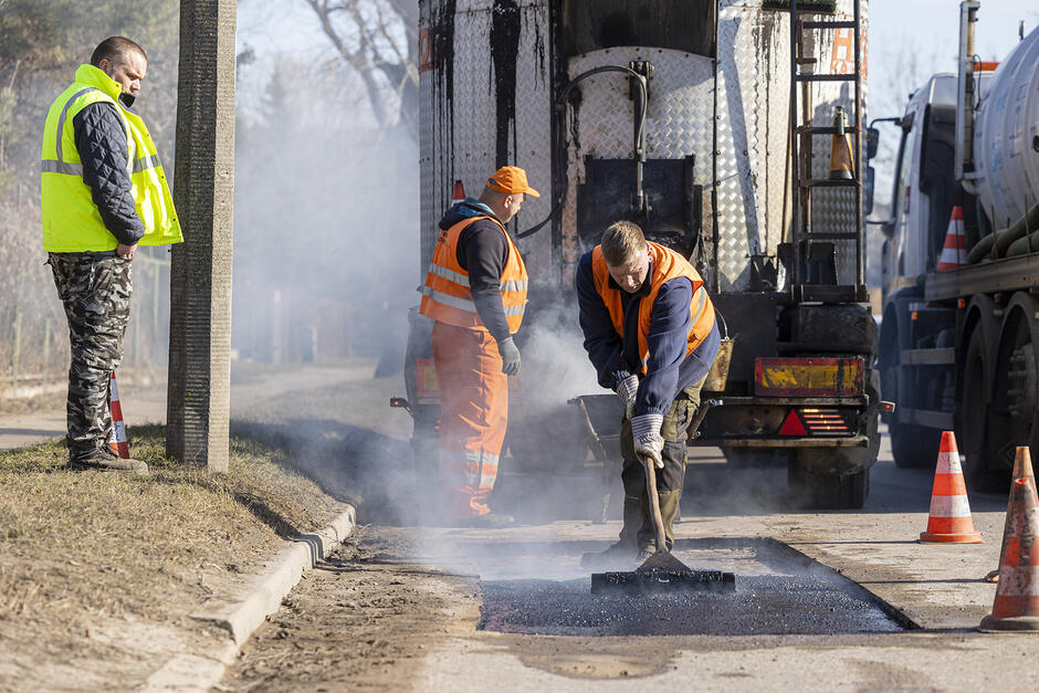 robotnicy układający asfalt na naprawianej jezdni, w tle duży samochód ciężarowy