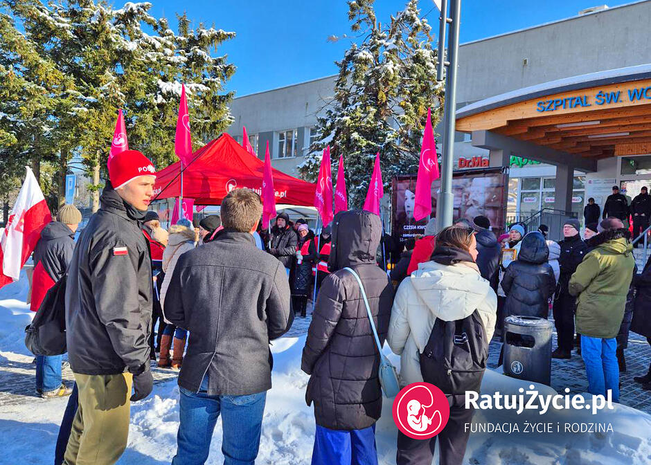 Grupa osób z transparentami i flagami pikietujących wejście do szpitala