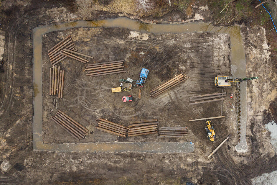 zdjęcie z drona widać plac budowy, koparki i wodę otaczającą plac budowy