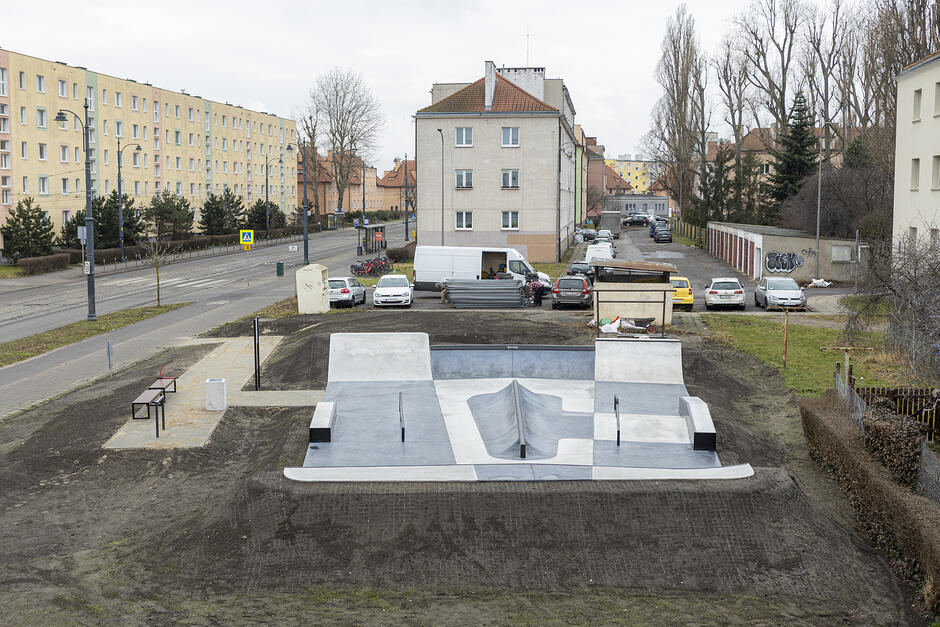 na pierwszym planie nowy, betonowy skejtpark, w tle kilka budynków mieszkalnych i ulica
