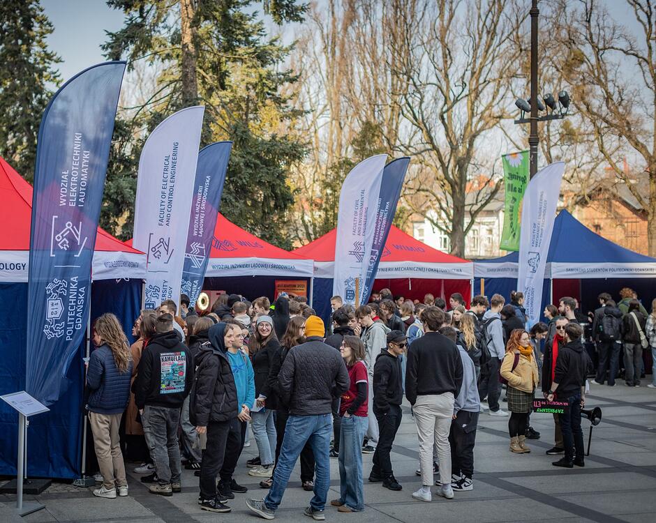 Politechnika Gdańska. Dzień otwarty. Ludzie stoją na dworze przy stoiskach. 