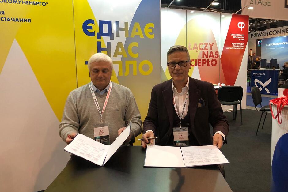 Dwaj mężczyźni siedzą podpisując jednocześnie na oddzielnych kartkach dokumentu