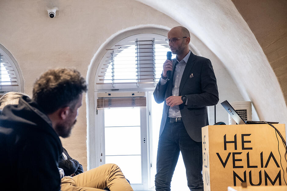 Mężczyzna z mikrofonem stoi obok mównicy w sali konferencyjnej.