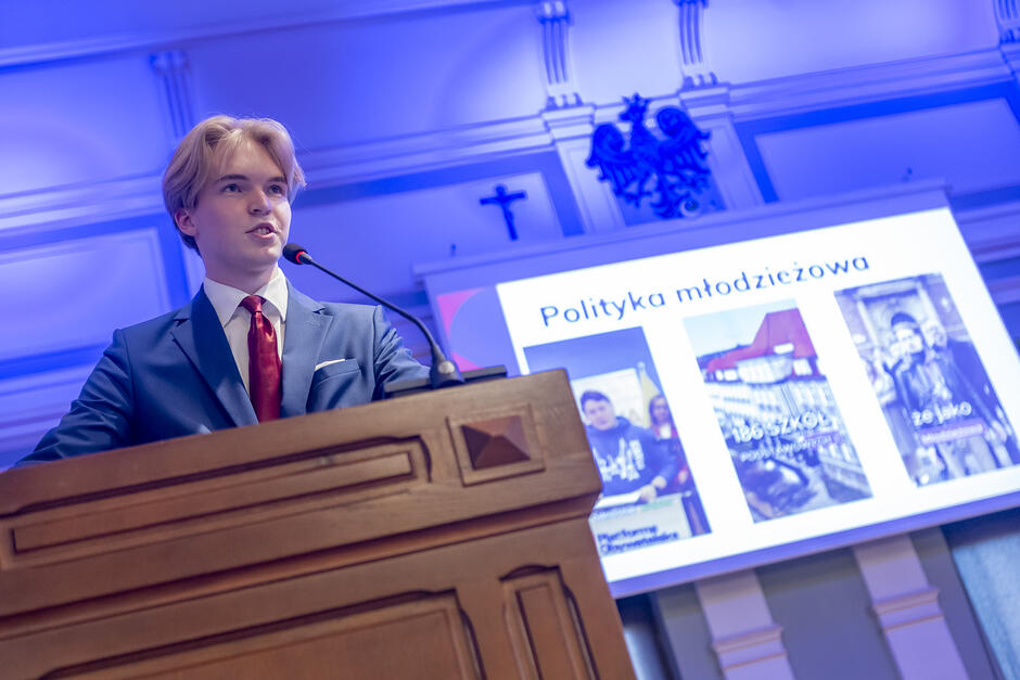 młody chłopak przemawia za drewnianą mównicą