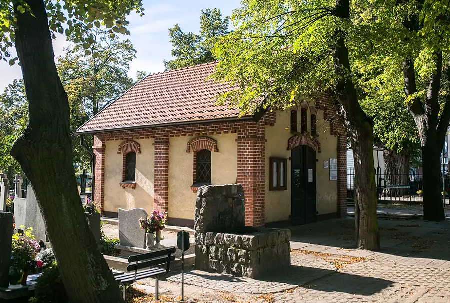 na zdjeciu kamienna studnia, w tle niewysoki budynek o jasnej elewacji