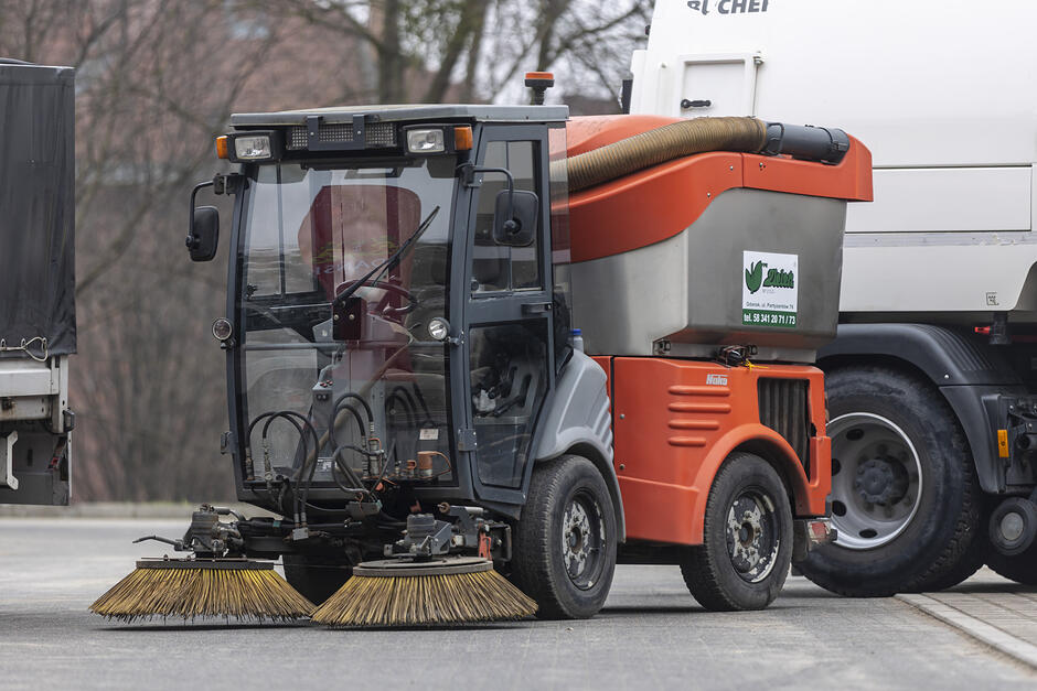 na zdjęciu nieduży pojazd z dwiema okrągłymi szczotkami przymocowanymi na wysokości kół pojazdu, służące do sprzątania ulic