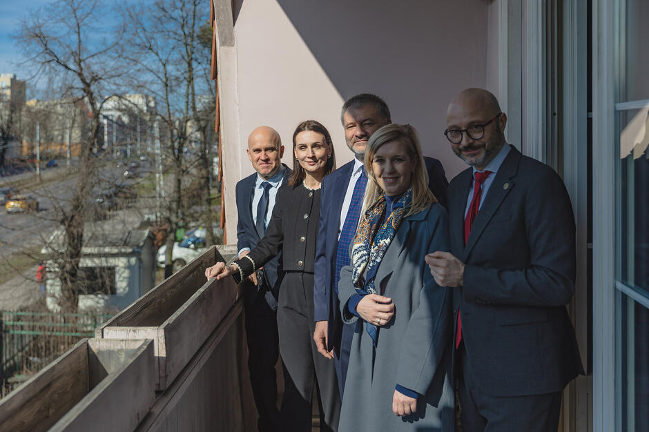 Dwie kobiety i trzech mężczyzn pozuje do zdjęcia na balkonie starego budynku.