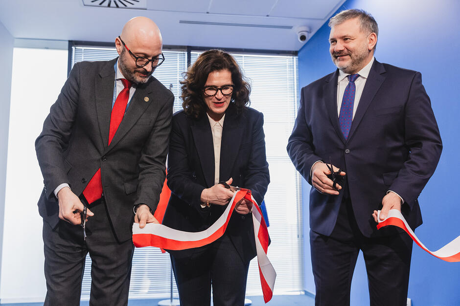 Kobieta i dwóch mężczyzn przecinają wstęgę w budynku.