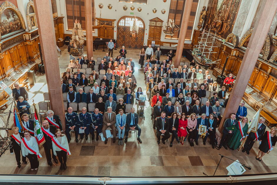 Kilkadziesiąt osób zebranych w reprezentacyjnej sali Dworu Artusa pozuje do zdjęcia robionego z wysokości.