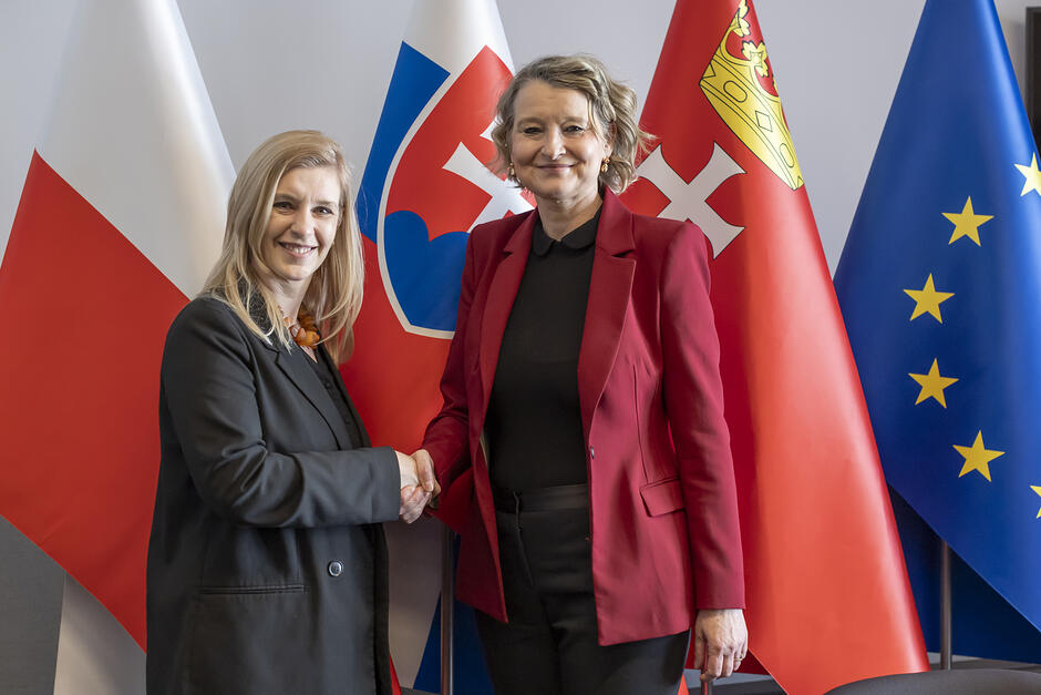 Dwie kobiety podają sobie rękę na tle flag Polski, Słowacji, Gdańska, Unii Europejskiej