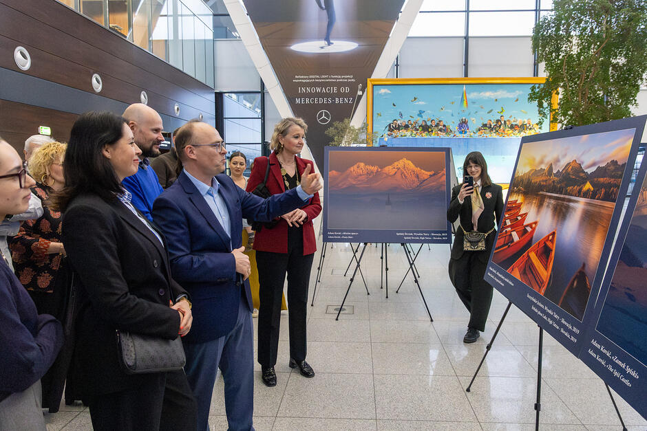 Grupa osób ogląda duże zdjęcia na statywach, z bliska widać dwa zdjęcia
