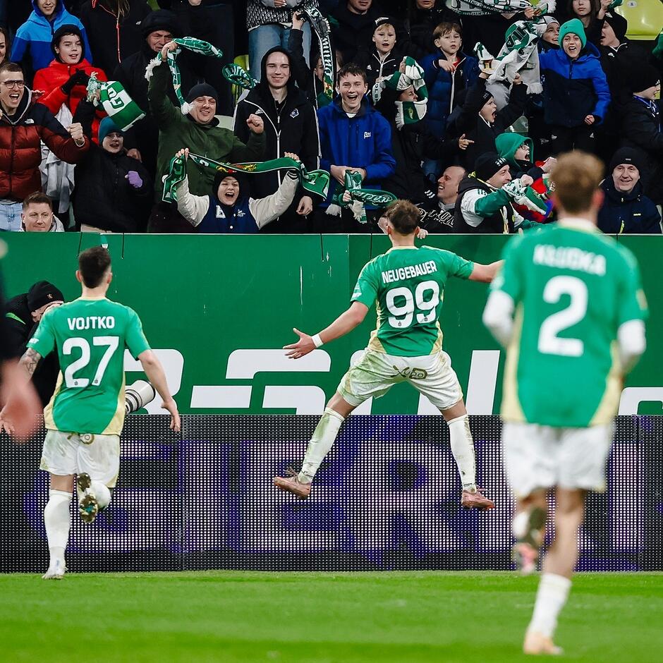 Zawodnicy na boisku cieszą się po zdobyciu bramki - w tle rozradowani kibice na trybunach