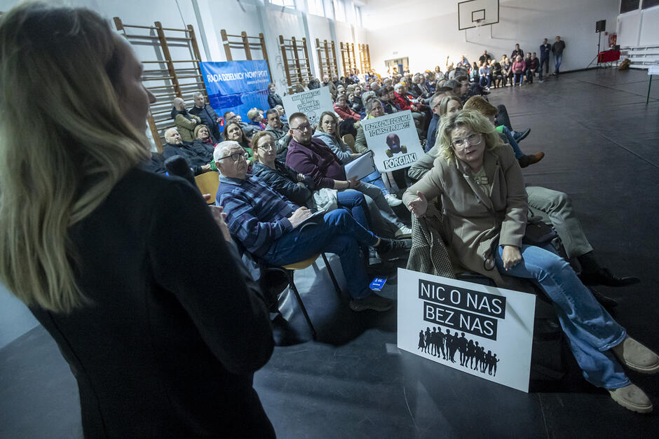 na zdjęciu szkolna sala gimnastyczna wypełniona tłumem ludzi, większość siedzi na krzesłach