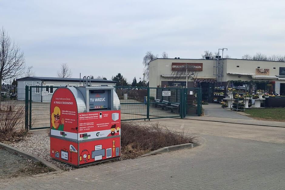 Pojemnik na elektroodpady obok bramy na cmentarz.