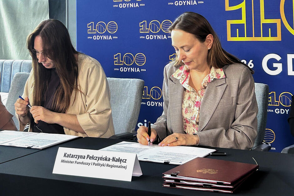 Dwie kobiety podpisują umowę siedząc przy stole.