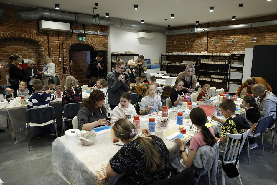 Dzieci siedzą przy stole, na którym znajdują się przedmioty do malowania