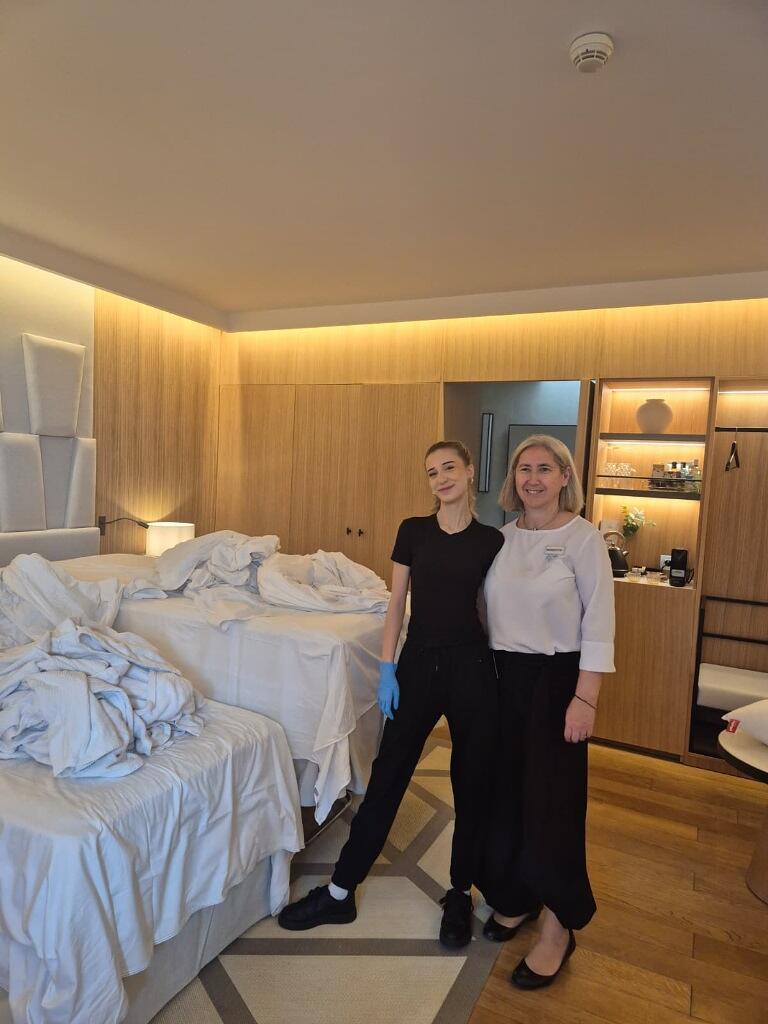 dwie kobiety - młoda i starsza, pozują w pokoju hotelowym, gdzie trwa wymiana pościeli