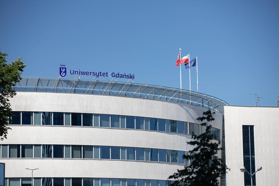 budynek uczelni z nazwą na szczycie i flagami Polski i Europy