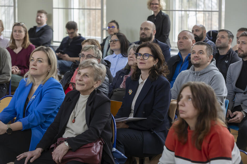 na zdjęciu grupa kilkunastu osób siedzi na krzesłach, patrzy przed siebie z zadartymi głowami, coś oglądają
