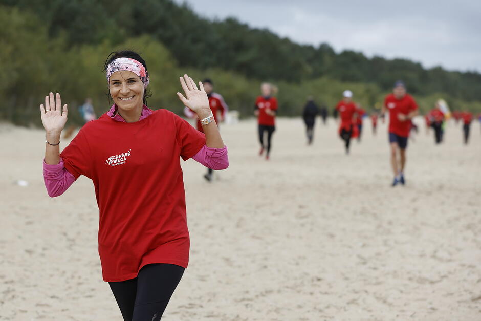 Kobiety w czerwonych koszulkach biegną po plaży