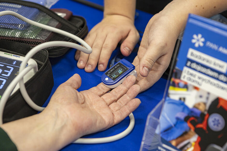 na zdjęciu dwie ludzkie dłonie, na jednej na placu założone jest urządzenie medyczne do mierzenia poziomu cukru we krwi