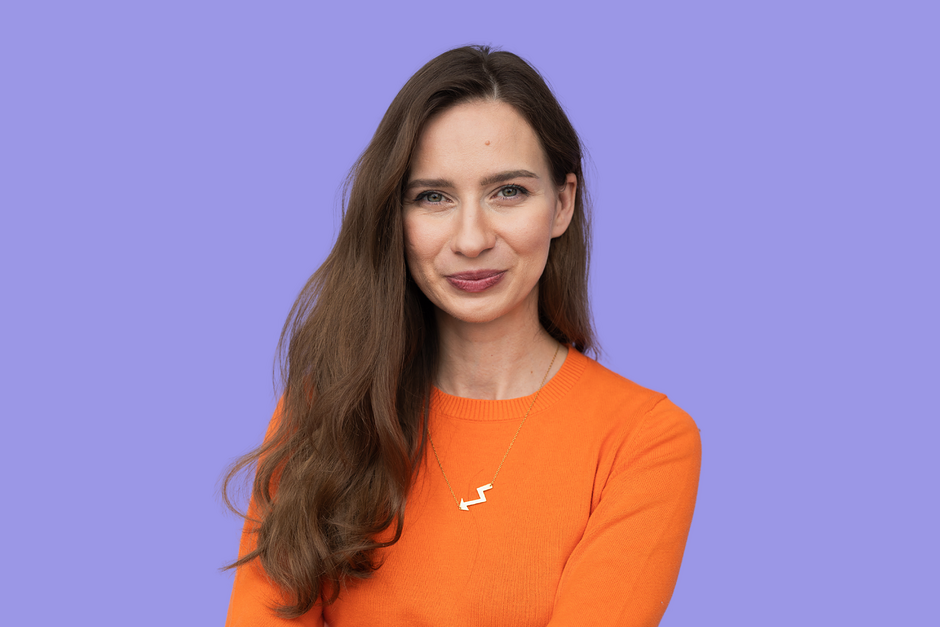 na zdjęciu uśmiechnięta kobieta z długimi włosami przed łokcie, w pomarańczowej bluzce 