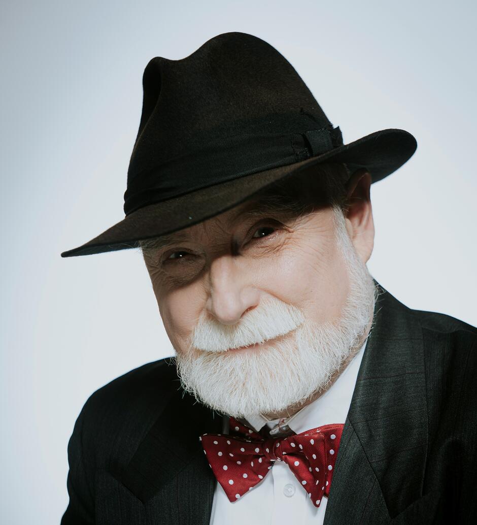 Na zdjęciu mężczyzna z siwym zarostem, na głowie czarny kapelusz.