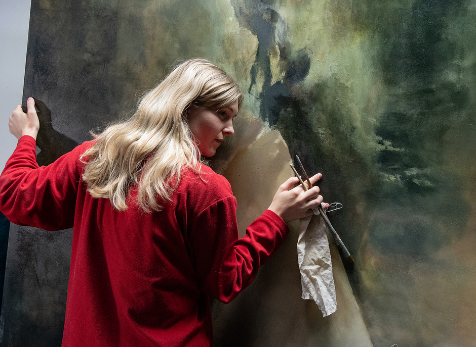 na zdjęciu kobieta w koszuli w odcieniach czerwieni, przytulająca się do dzieła plastycznego.