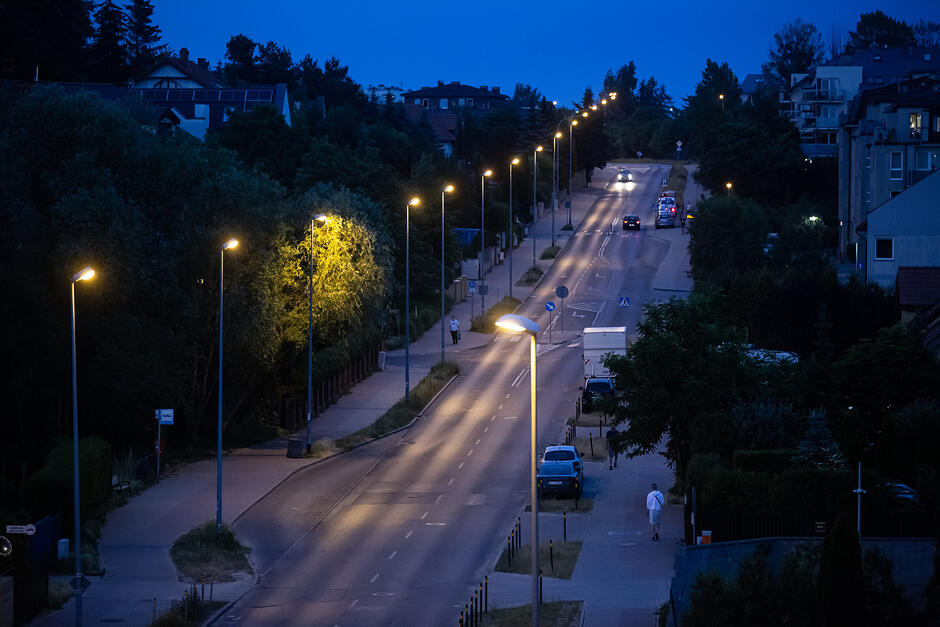 zdjęcie ulicy po zmroku, widać świecące latarnie uliczne, ulicą jadą samochody
