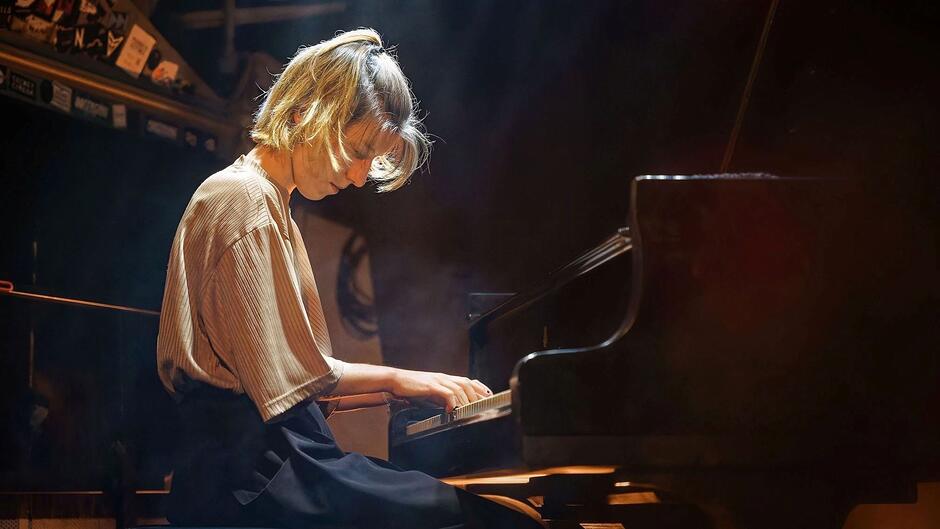 Na zdjęciu kobieta o jasnych włosach, pochylona nad instrumentem klawiszowym.