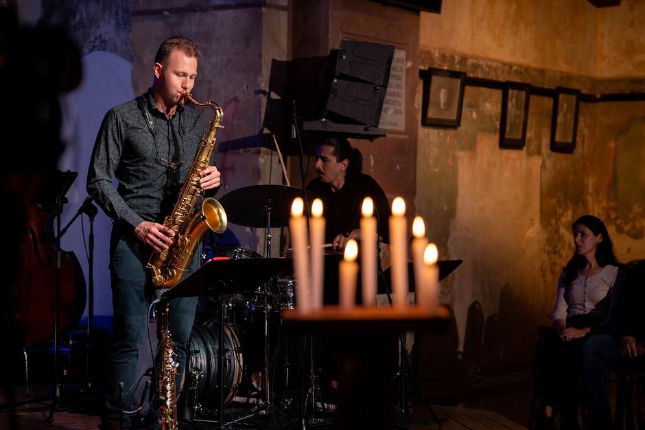 na zdjęciu mężczyzna grający na saksofonie, w tle rozpalone świece