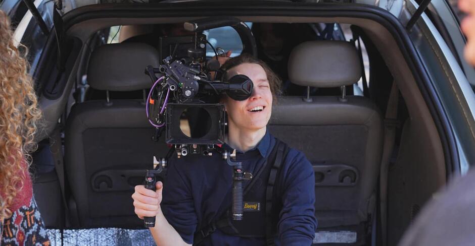 Na zdjęciu mężczyzna trzymający w rękach kamerę, siedzący w bagażniku auta.
