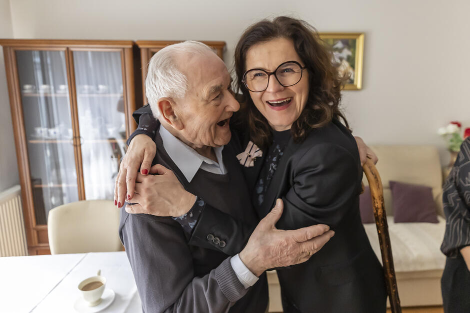 Stary mężczyzna i dużo młodsza kobieta obejmują się i śmieją.