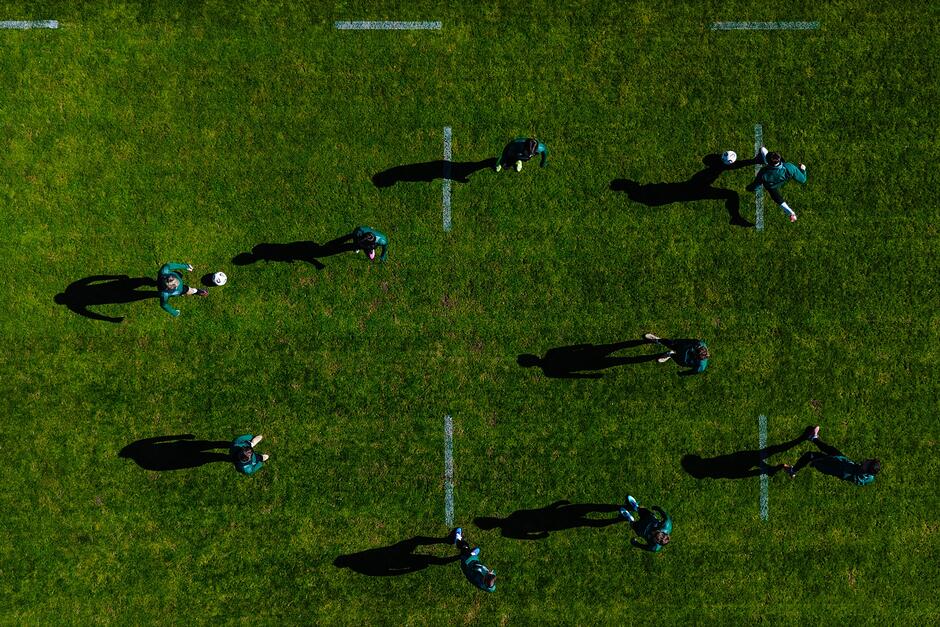 Widok boiska zrobiony z wysokości drona, pionowa. W dole widać sylwetki piłkarzy i pikę