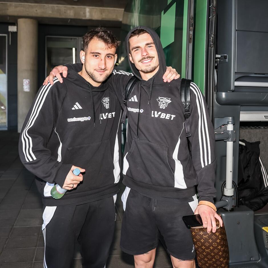 Dwaj zawodnicy w braterskim uścisku, pozują do zdjęcia przy burcie klubowego autokaru