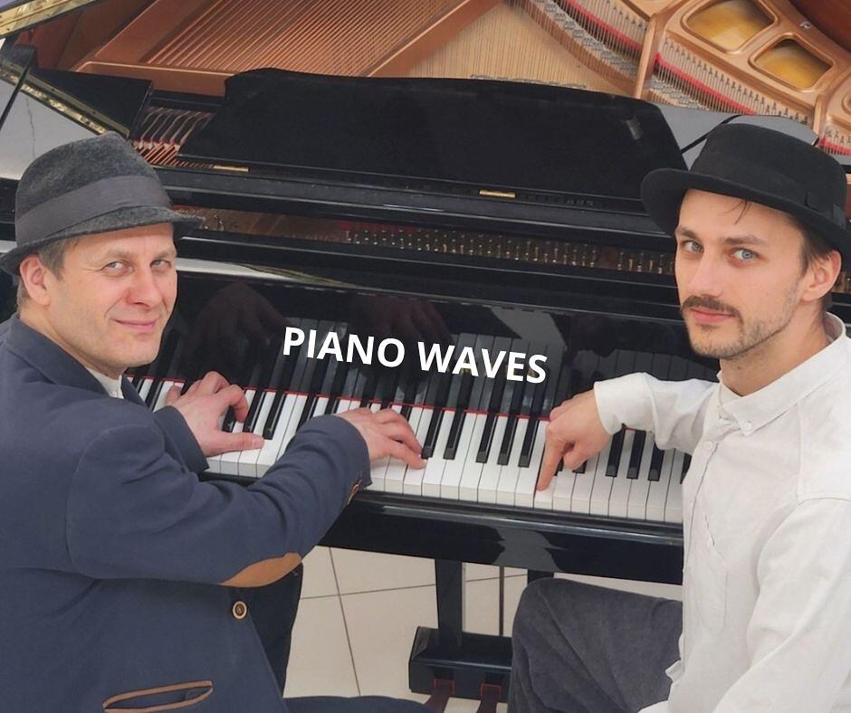 Na zdjęciu dwóch mężczyzn w kapeluszach grających na instrumencie klawiszowym. Na instrumencie napis PIANO WAVES.