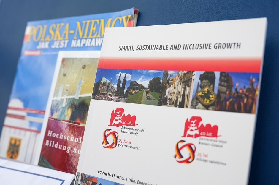 Zdjęcie przedstawia okładki publikacji dotyczących współpracy polsko-niemieckiej oraz partnerstwa miast Brema i Gdańsk. Na pierwszym planie widoczna jest broszura o tytule „Smart, Sustainable and Inclusive Growth”, opatrzona logotypami upamiętniającymi jubileusze wspólnych relacji. 