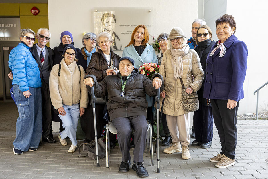 Grupa kilkunastu osób w różnym wieku, pozują do zdjęcia stojąc pod tablicą