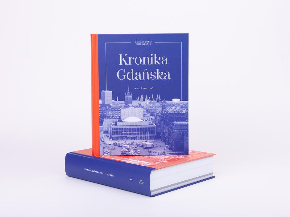 Gruba księga sfotografowana w studiu fotograficznym na jasnym tle. Na leżącej księdze stoi kolejna.