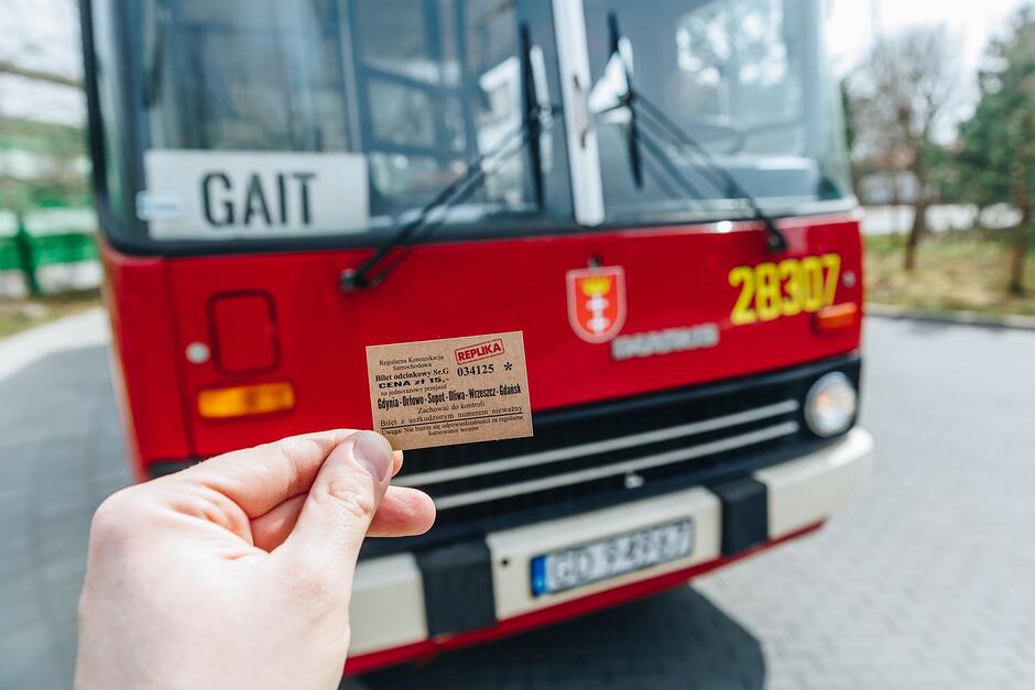 Zabytkowy bilet trzymany w ręku na tle czerwonego Ikarusa