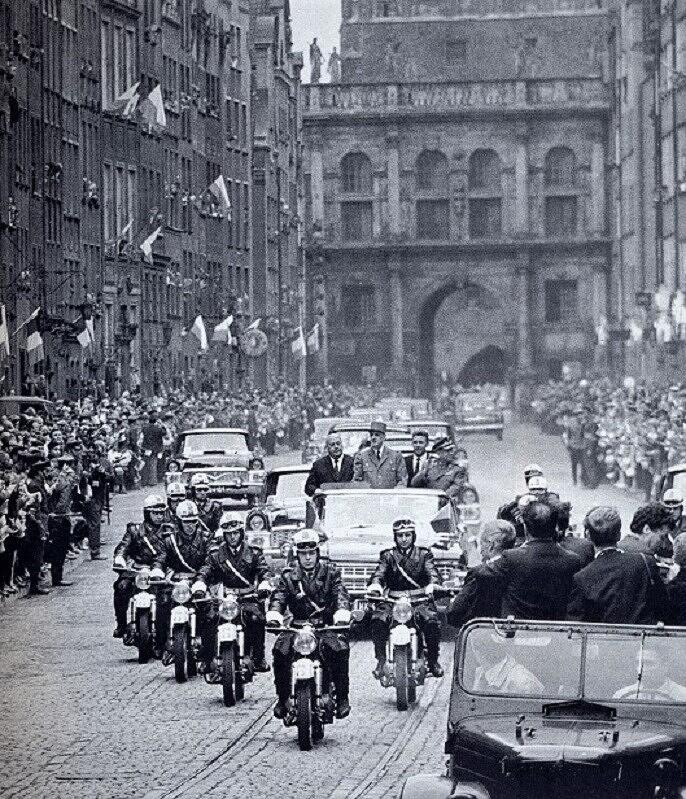 Kolumna samochodów jedzie środkiem ulicy Długiej, w tle widać Złotą Bramę