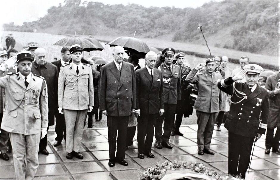 Generał de Gaulle w otoczeniu około 20 osób, w tle widać krzyże cmentarza wojskowego