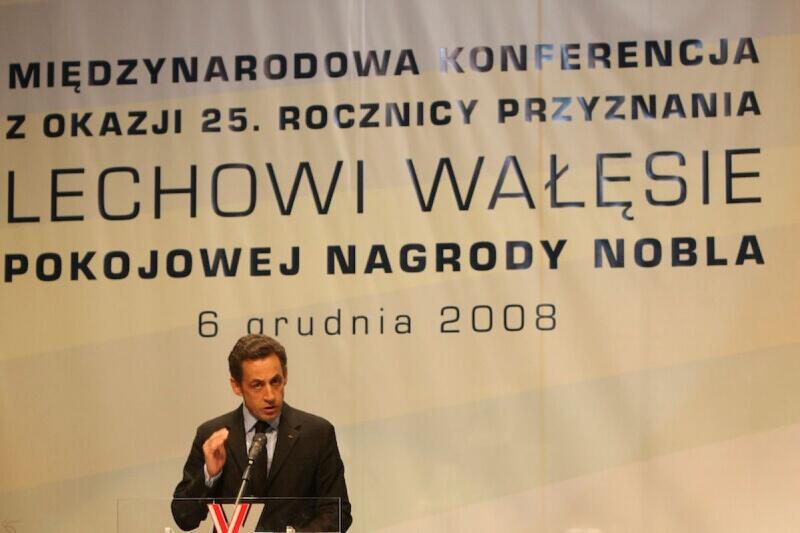 Prezydent Francji siedzi za stołem konferencyjnym, przemawiając do uczestników uroczystości
