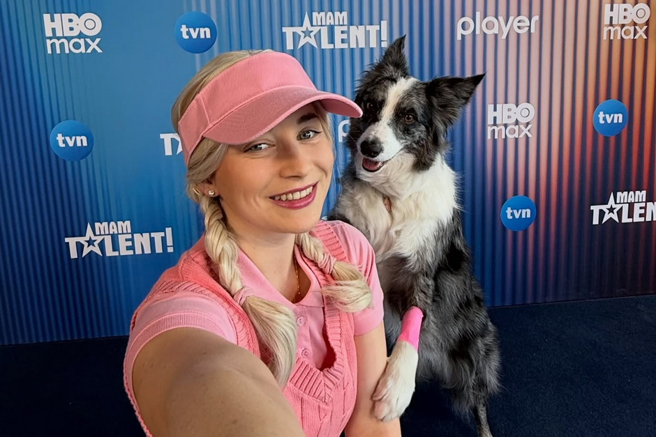 Dziewczyna i pies pozują do zdjęcia na tle niebieskiej ścianki. Są w różowych strojach. 