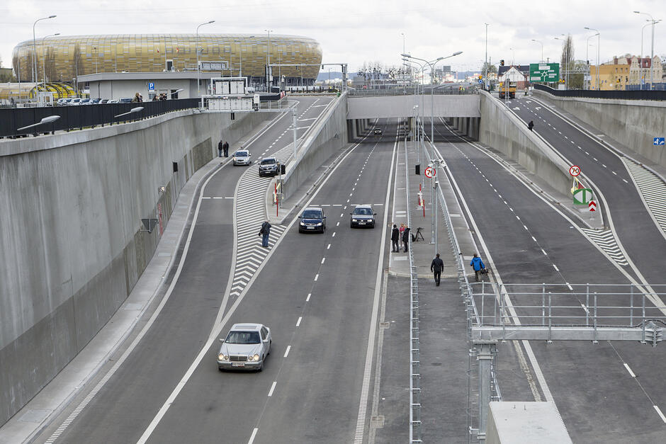Wyjazd z tunelu drogowego. Po jezdni jadą samochody. W tle stadion.