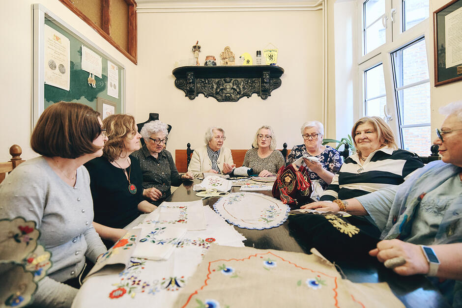 Kobiety siedzą przy stole i haftują