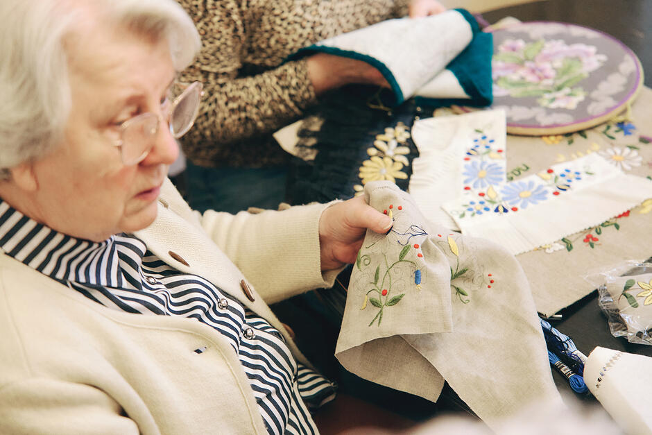 Kobieta w okularach trzyma materiał, na którym haftuje