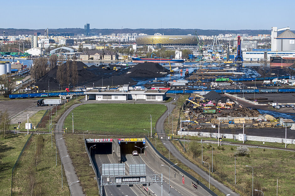 Wjazd do tunelu drogowego, dalej infrastruktura przemysłowa, hałdy węgla, rzeka. W tle stadion piłkarski. 