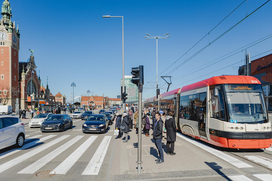 Przystanki tramwajowe, piesi stoją na przejściu dla pieszych, samochody jadą